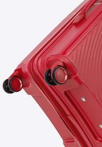 Maleta dura roja con líneas en relieve, textura suave, ruedas giratorias dobles y un cierre de cremallera duradero.