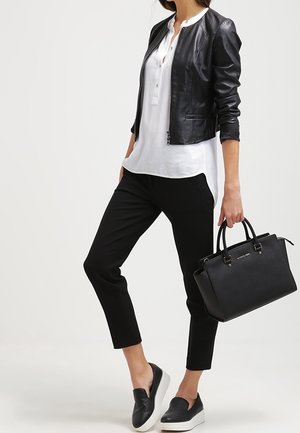 Giubbotto bomber in pelle nera sopra una camicia bianca con bottoni, pantaloni neri alla caviglia e scarpe slip-on nere. Borsa nera con doppi manici.