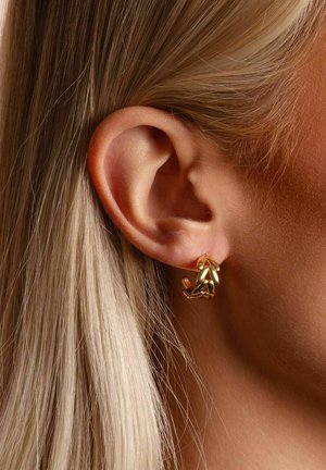 Close-up of a left ear with blonde hair wearing a small gold leaf-shaped hoop earring.