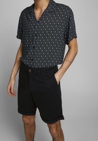 Svartvit skjorta med diamantmönster och korta ärmar, matchad med svarta shorts med uppvikta fållar och framknäppning.