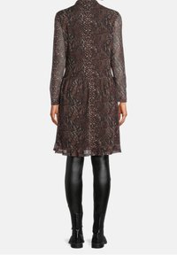 Abito brown a stampa serpente con maniche lunghe in organza, corpetto aderente e gonna svasata. Abbinato a leggings in pelle nera e stivaletti.
