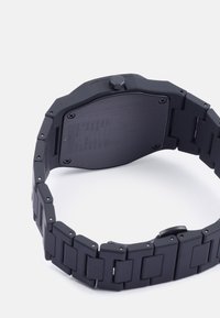 Relógio preto com acabamento mate e elos retangulares na bracelete. A parte de trás é plana com detalhes gravados e uma coroa proeminente de um lado.