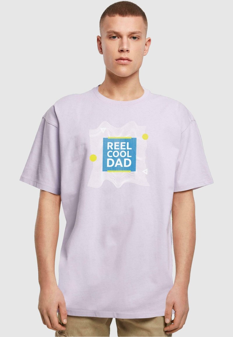 Camiseta de algodón de color púrpura claro con un gráfico de cuadrado azul que lleva el texto "REEL COOL DAD", acentuado por puntos amarillos y líneas blancas onduladas.