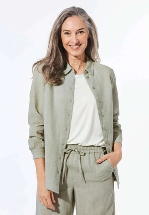 Chemise en lin vert clair à boutons, portée par-dessus un top blanc. Associée à un pantalon léger assorti, doté d'une taille élastique et d'un cordon de serrage.