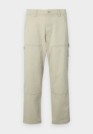 Beige cargo bukser laget av bomull med flere lommer, forsterkede knær og rette ben. Har en knappelukking og beltehemper.