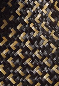 Vevd kurv med et mønster av svarte og lysebrune materialer, med en glatt, teksturert overflate og et diagonalt flettet design.