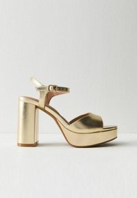 Guldmetalliska högklackade sandaler med bred plattform, öppen tå, ankelrem och vadderad sula för komfort.