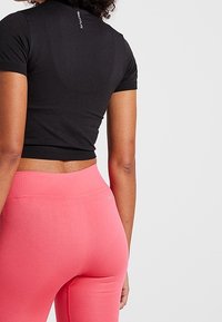 Černé crop tričko s přiléhavými krátkými rukávy, doplněné růžovými legínami s vysokým pasem, které mají hladkou texturu a minimalistický design.