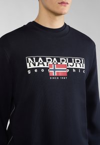 Felpa blu navy con colletto a coste, presenta il logo bianco "NAPAPIJRI" e un'emblema della bandiera norvegese rossa e blu. Design semplice e pulito.