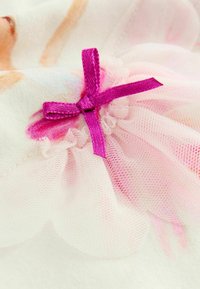 Lila Satin-Schleife, die an einem weichen rosa Tüllstoff mit gewellten Kanten auf einem hellen Stoffhintergrund befestigt ist.