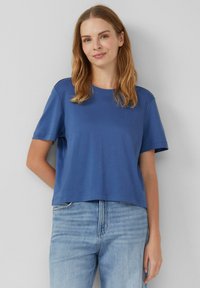 T-shirt bleu à manches courtes en tissu doux avec un col rond et une coupe décontractée, associé à un jean en denim délavé.