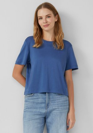 T-shirt bleu à manches courtes en tissu doux avec un col rond et une coupe décontractée, associé à un jean en denim délavé.