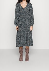 Kukallinen midi-mekko, jossa on pitkät hihat, V-pä�äntie, gathered-vyötärö, tummansininen pohja ja pieniä monivärisiä kukkia. Yhdistetty vaaleanruskeisiin löysiin saappaisiin.