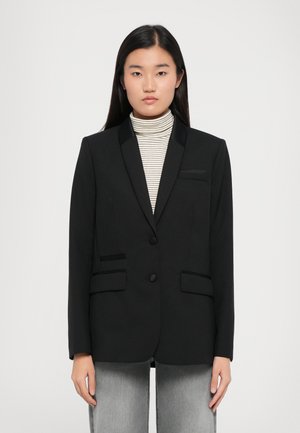 Black blazer with satin lapels, two front pockets, and button closure. Worn over a striped turtleneck. Smooth texture, structured fit.