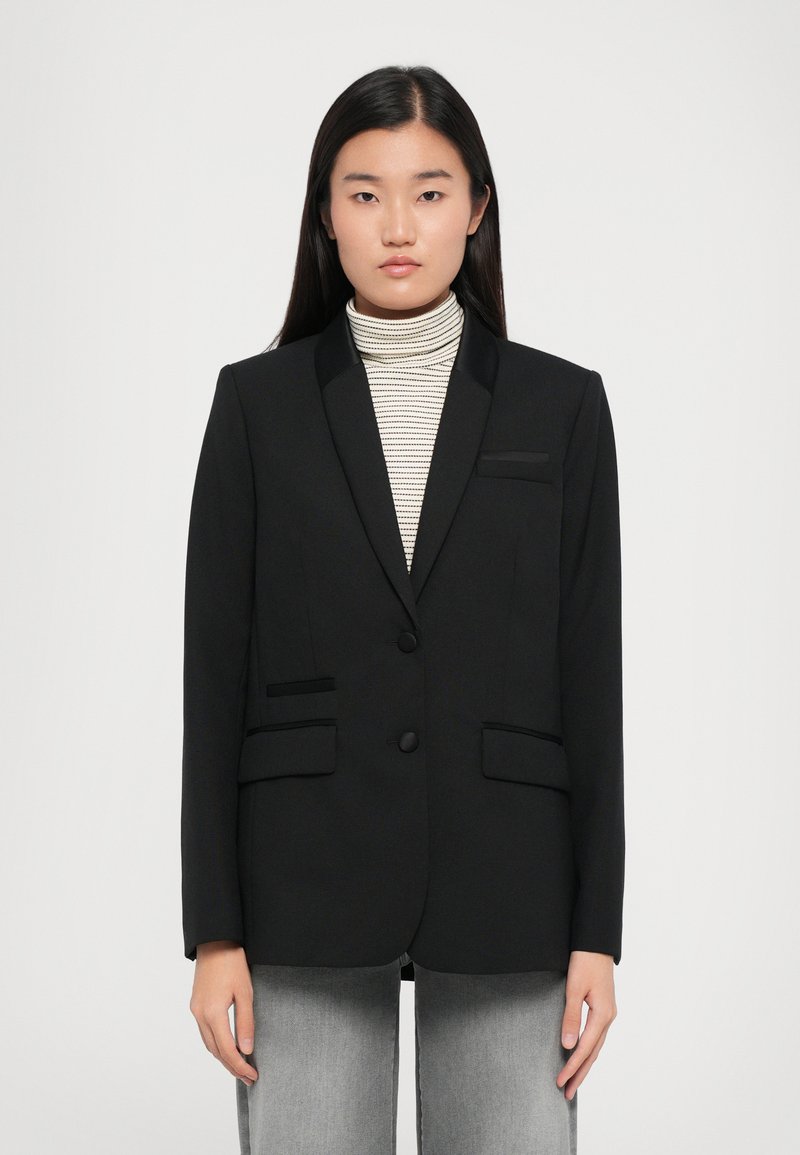 Black blazer with satin lapels, two front pockets, and button closure. Worn over a striped turtleneck. Smooth texture, structured fit.