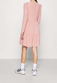 Abito rosa a maniche lunghe con texture a costine, gonna a strati e dettagli raccolti sulle spalle, abbinato a calze bianche e sneakers multicolori.