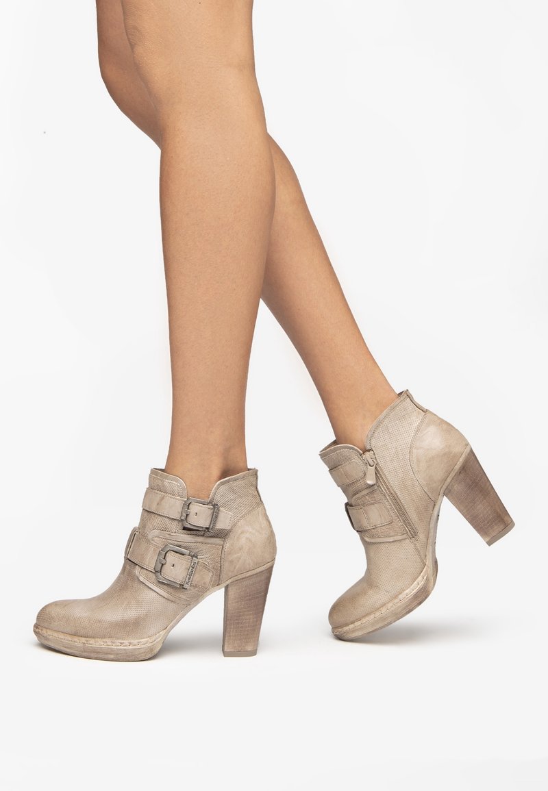 Botas cortas beige hechas de cuero texturizado con dos grandes hebillas, tacón robusto y punta redondeada. Cierre lateral con cremallera para facilitar su uso.