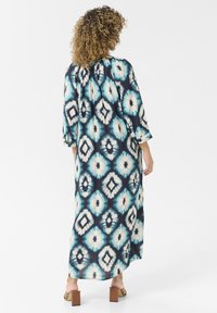 Rochie lungă și fluidă cu un fundal marin, având un model geometric mare, alb și turcoaz. Fabricată dintr-un material ușor.
