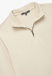 Beżowa bluza z zamkiem błyskawicznym i kołnierzykiem polo, wykonana z miękkiego materiału. Posiada zamek z przodu oraz ściągacz na kołnierzu, o gładkiej fakturze.