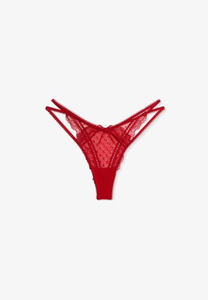 Culotte string en dentelle rouge avec double bandeau à la taille, tissu transparent à pois, bords ondulés et petit nœud au centre devant.