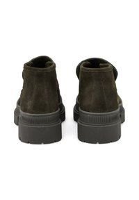 Bottes chelsea en suede vert foncé avec une semelle en caoutchouc texturé, présentant des bords arrondis et des détails de couture minimaux à l'arrière.