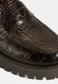 Krokodillenleer bruine loafer met een gestructureerde afwerking, voorzien van een stevige rubberen zool en een decoratieve band over het bovenwerk.