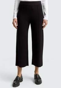Wijde zwarte broek gemaakt van textuurstof, met een hoge taille en voornaad. Gepaard met chunky zwarte loafers.
