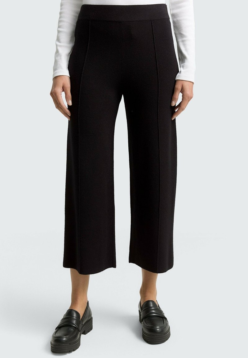 Pantalons noirs à jambe large en tissu texturé, dotés d'une taille haute et de coutures avant. Associés à des mocassins noirs épais.