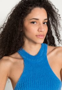 Top halter azul, felpudo, com uma textura canelada e um decote redondo, apresentando um logotipo discreto bordado perto do pescoço.