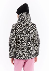 Mustekäsitelty musta ja kreemivärviga zebra-mustriga puffjakkk, millel on kapuuts, elastsed mansetid ja vabalt laskuv lõige, kantud roosade pantide peal.