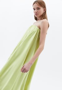 Schnürsenkelloses Kleid aus hellgrünem Satin, fließendes Design mit sanften Drapierungen und dezentem Glanz. Es hat eine lockere Passform und keine sichtbaren Verschlüsse.
