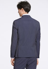 Mörkblå randig kostymjacka med en strukturerad design, enkel ventil, insnitna slag och fyra knappar vid ärmsluten.