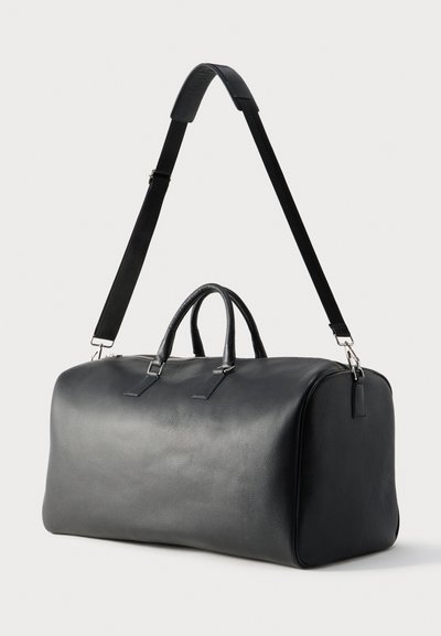 Borsa da viaggio in pelle nera con doppi manici e tracolla regolabile e removibile su sfondo bianco.