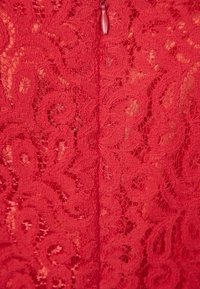 Röd spets tyg med intrikata blommönster, med en mittsöm och en liten dragkedjedetalj bak.