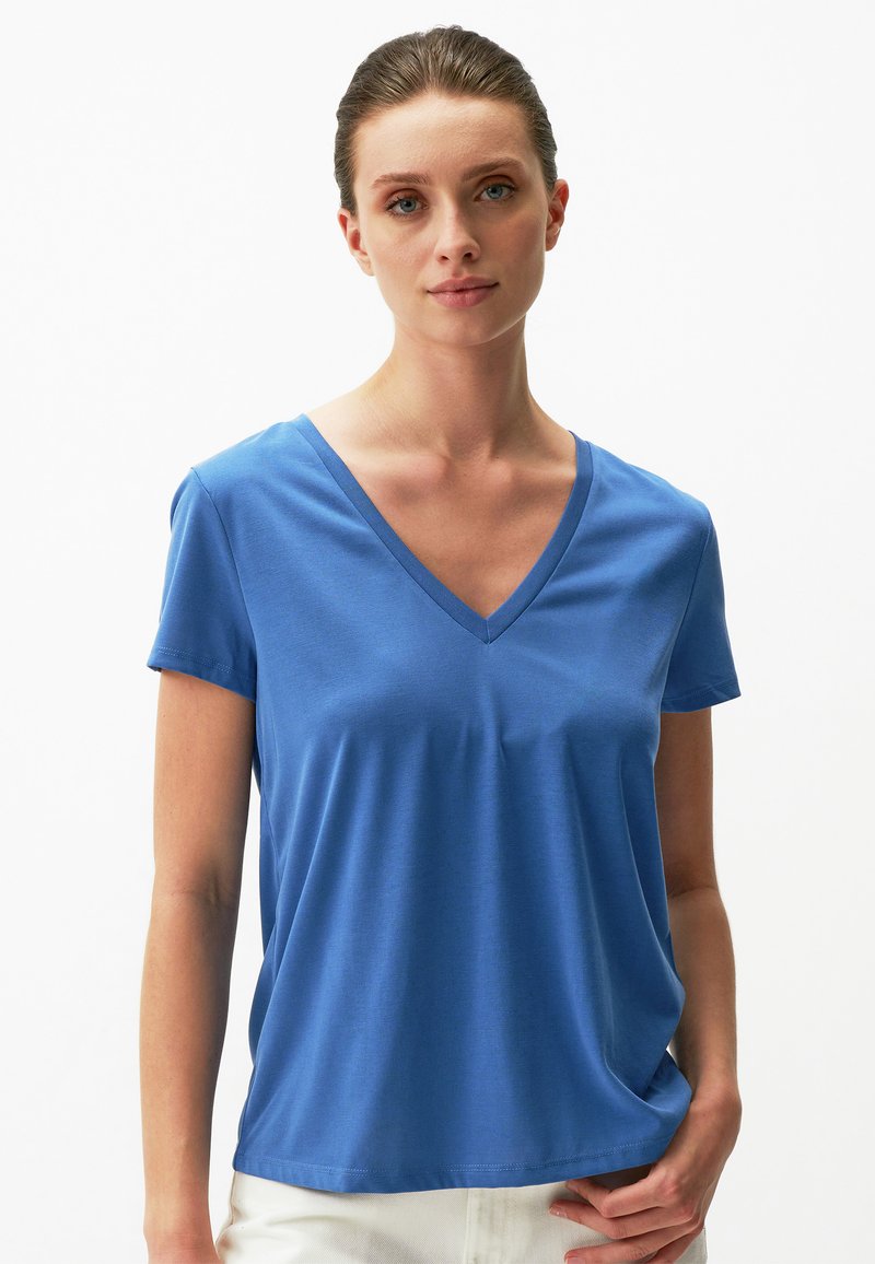 Niebieska koszulka z dekoltem w serek, wykonana z miękkiego, lekkiego materiału, z krótkimi rękawami i luźnym krojem, o gładkiej fakturze i subtelnych detalach podczas szycia.