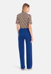 Multicolored patterned short-sleeve top paired with royal blue, high-waisted wide-leg pants, featuring a smooth texture and tailored design.