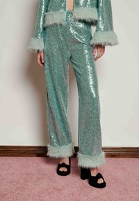 Shiny, teal sequin outfit with faux fur trim on sleeves and pant legs; wide-legged pants paired with black platform shoes.