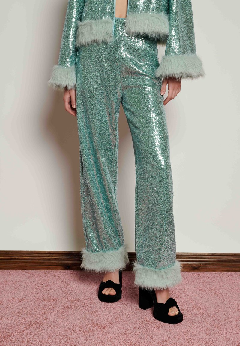 Shiny, teal sequin outfit with faux fur trim on sleeves and pant legs; wide-legged pants paired with black platform shoes.