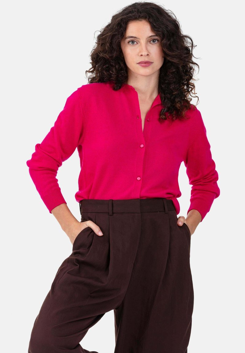 Fuchsiafarbener Cardigan mit durchgehendem Knopfverschluss, gerippten Bündchen und Kragen, kombiniert mit hoch taillierter brauner Hose mit seitlichen Taschen.