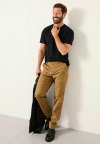 Schwarzes Kurzarm-T-Shirt, kombiniert mit beigen Chinos, strukturiertes Material, Slim Fit und schwarzen Stiefeletten. Stehende Pose vor einem hellen Hintergrund.