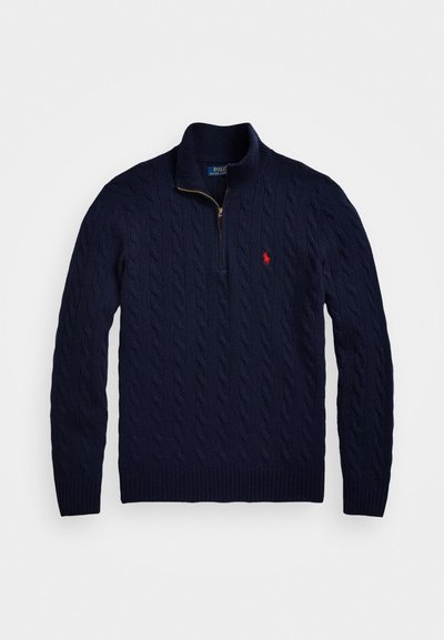 Granatowy sweter w splot kablowy z półzamknięciem przy kołnierzu i małym czerwonym wyhaftowanym logo na piersi.