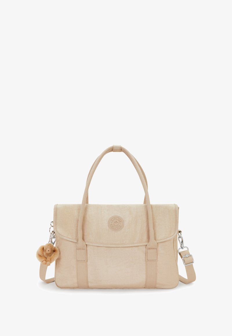 Sac en tissu beige avec une fermeture à rabat, des poignées courtes et une bandoulière ajustable. Présente un logo rond et un charm en peluche attaché.