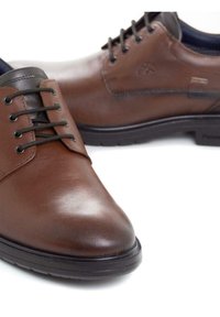 Zapatos de cuero marrón con un acabado suave, con punteras redondas, cordones negros y un ribete oscuro en contraste a lo largo de los bordes. Suela de goma.