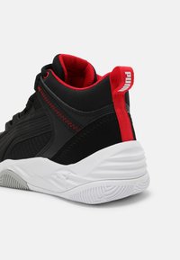 Baskets montantes noires avec des panneaux texturés et des accents rouges. Elles disposent d'une semelle blanche avec des stries et d'une languette rayée étiquetée "PUMA".