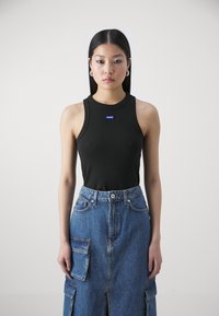 Black ribbed sleeveless top with a round neckline featuring a small blue 'Hugo' label, paired with a long blue denim skirt with pockets.