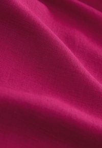 Tessuto magenta liscio con trama visibile e pieghe morbide che creano ombre e riflessi diagonali.