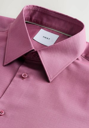 Kortärmad skjorta i ljusrosa, med ett strukturerat mönster, spetsig krage och matchande rosa knappar. Lappen visar "NEXT."