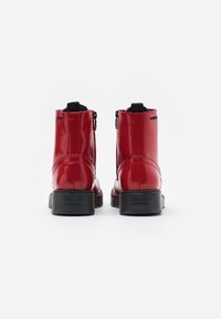 Botines de charol rojo con un acabado suave, paneles laterales elásticos y suelas de goma negra. Cuenta con una lengüeta en la parte trasera para facilitar su uso.