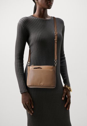 Vrouw draagt een grijze jurk met lange mouwen en ribbelstructuur, een beige doorgestikte crossbodytas en een dikke gouden armband aan haar rechterpols.