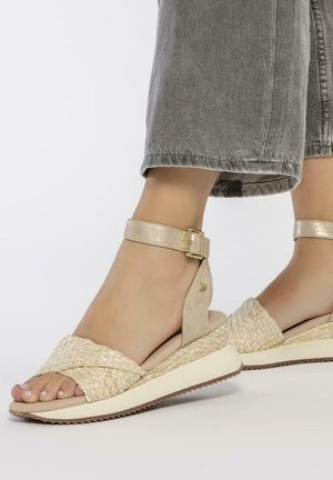 Sandalias de paja trenzada con una paleta de colores beige y dorado, que cuentan con una correa en el tobillo con un hebilla metálica y una suela de plataforma.